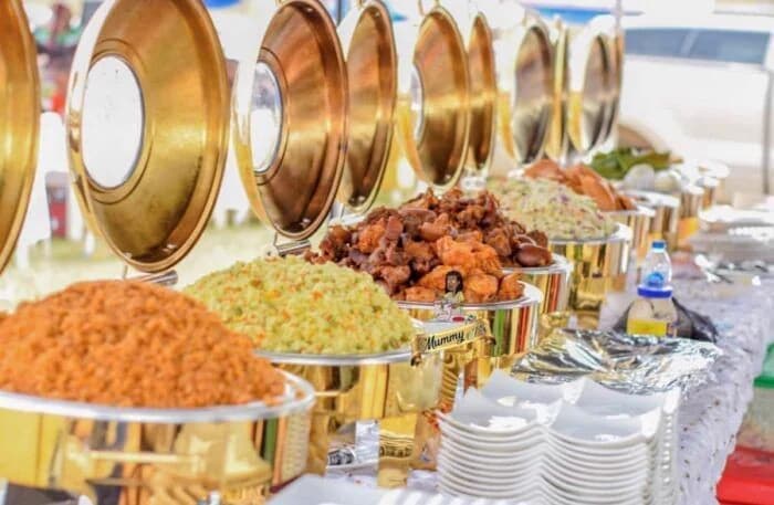 A gold chafing dish buffet set up for an event with jollof rice, fried rice and peppered meat
