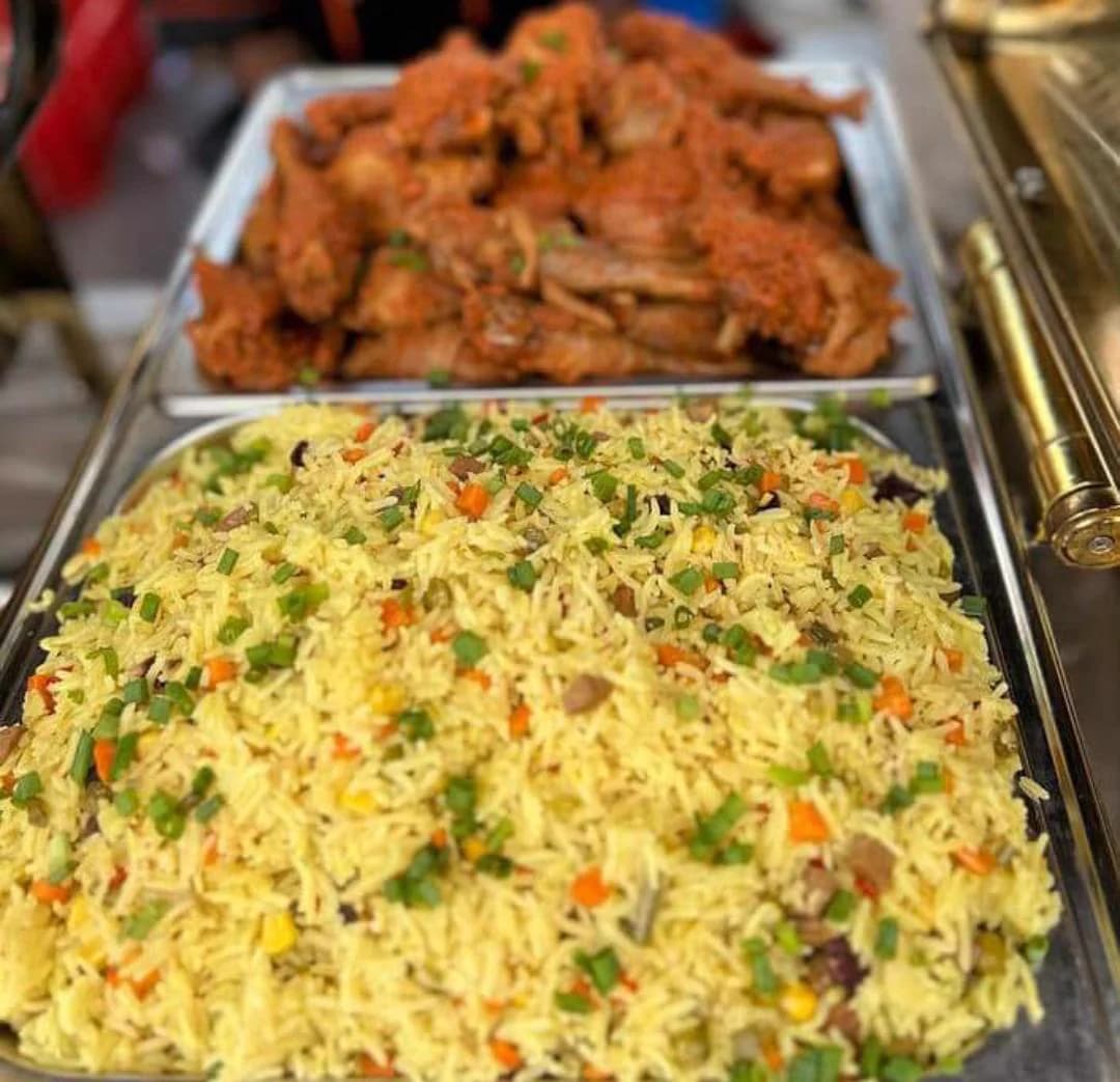Fried rice garnished with spring onion beside a tray of peppered chicken in chafing dishes