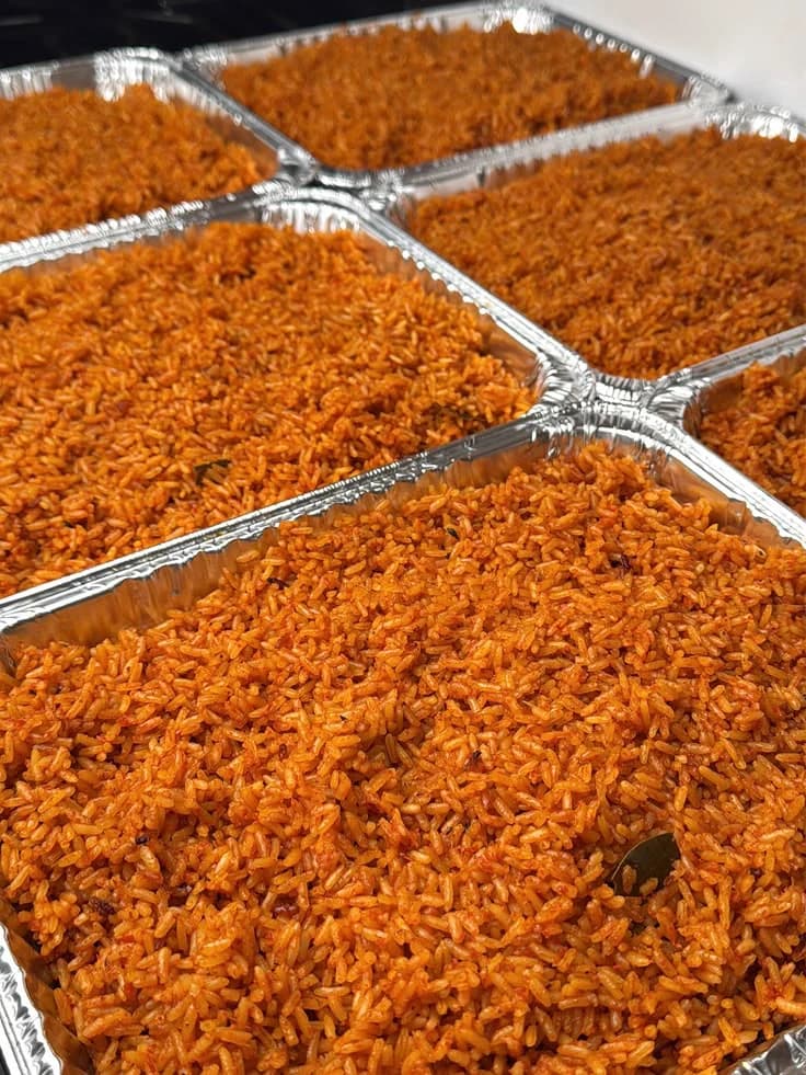 Several foil food trays filled with freshly cooked jollof rice