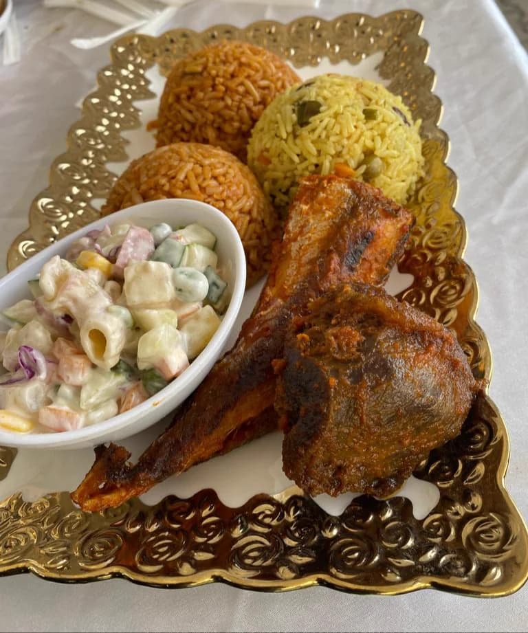 An event plate on a gold charger holding jollof rice, fried rice, coleslaw and grilled fish